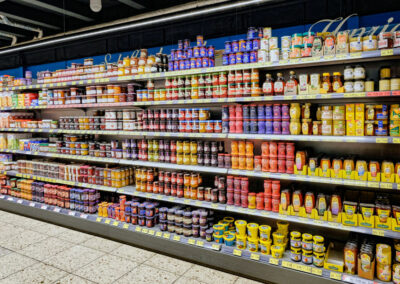 Supermarktregal mit vielen Gläsern und Flaschen, darunter Marmelade, Honig und Frühstücksaufstriche.
