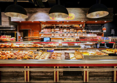 Bäckereitheke im Supermarkt mit Broten, Brötchen und Gebäck unter großen Lampen.
