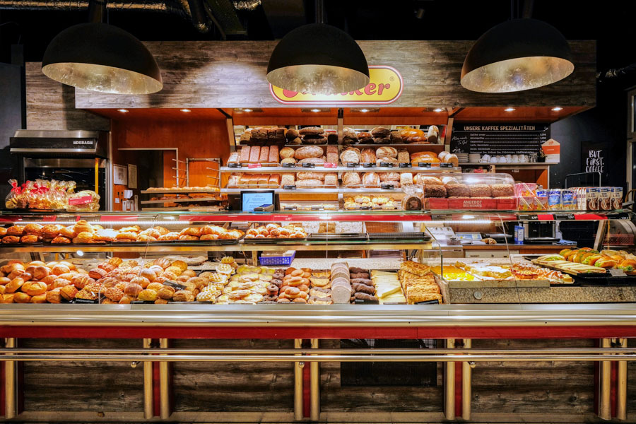 Bäckereitheke im Supermarkt mit Broten, Brötchen und Gebäck unter großen Lampen.