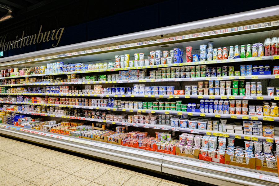 Großes Kühlregal im Supermarkt mit Joghurt, Desserts und Milchprodukten.