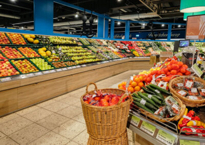 Obst- und Gemüseabteilung im Supermarkt mit gefüllten Regalen und Körben voller frischer Ware.