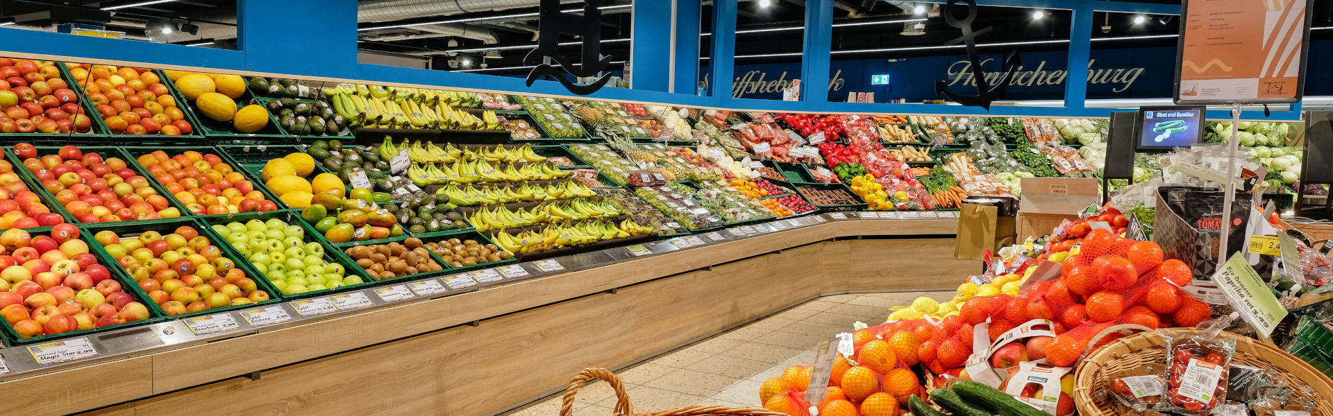 Obst- und Gemüseabteilung im Supermarkt mit gefüllten Regalen und Körben voller frischer Ware.