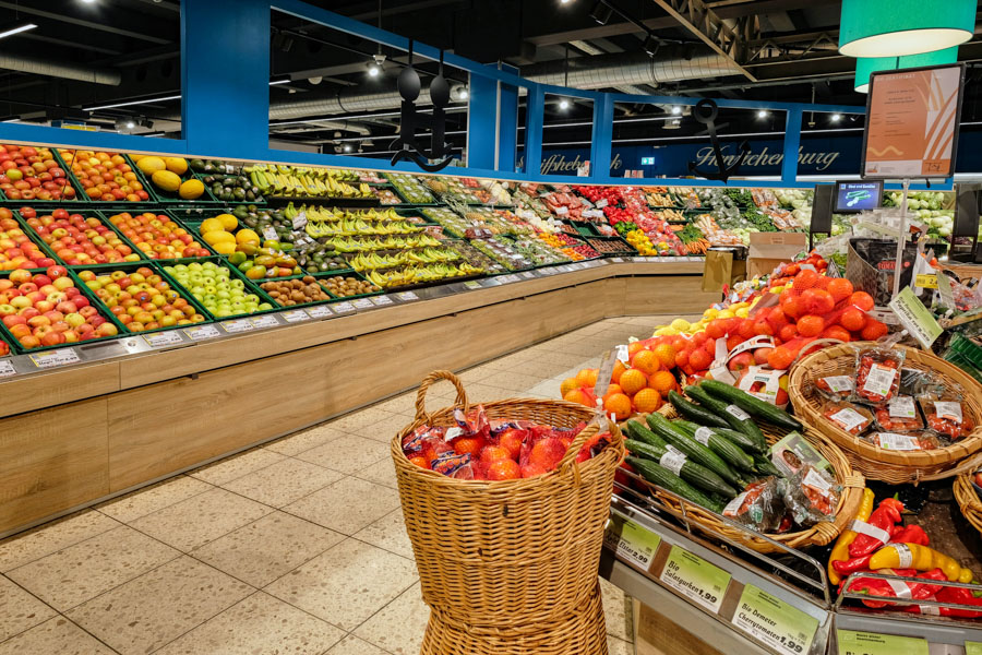 Obst- und Gemüseabteilung im Supermarkt mit gefüllten Regalen und Körben voller frischer Ware.