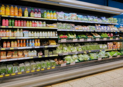 Kühlregal im Supermarkt mit Säften, Milchgetränken, Salaten und frischem Gemüse.
