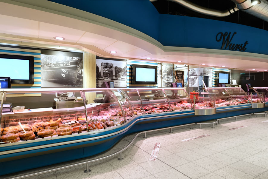 Lange Fleischtheke im Supermarkt mit Wurst- und Fleischwaren hinter Glas.