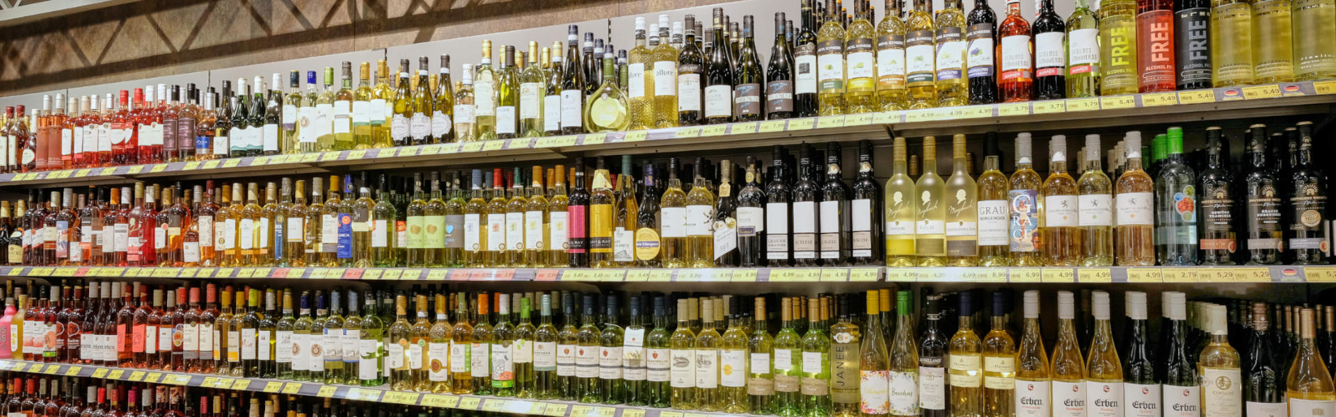 Langes Weinregal im Supermarkt mit vielen Flaschen und dem Schild „Spirituosen“.